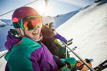 a smiling snowbaorder riding the lift to the alpine with 2 skiers